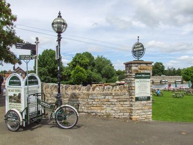 An outdoor area with signs for Avon Boating near a river with picnic tables and a stone wall at Highcroft in Stratford-Upon-Avon