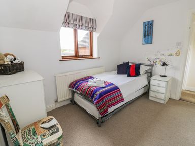 A bedroom with a single bed a striped blanket and pillows a window a chair a chest of drawers and a nightstand at Highcroft in Stratford-Upon-Avon