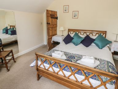 A bedroom with a wooden bed with pillows and towels a wooden door a wooden chair and a large mirror at Highcroft Stratford-Upon-Avon