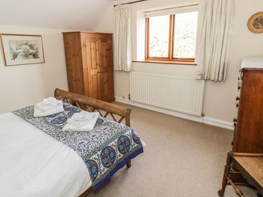 A bedroom with a wooden bed, wardrobe, chest of drawers and a window at Highcroft in Stratford-Upon-Avon