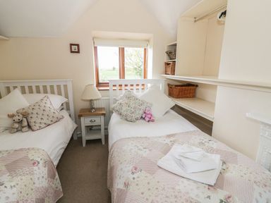 A bedroom with two single beds a nightstand with a lamp and shelves with baskets at Highcroft Stratford-Upon-Avon
