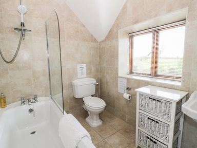 A bathroom with a bathtub shower toilet wicker drawers and a window with blinds at Highcroft Stratford-Upon-Avon