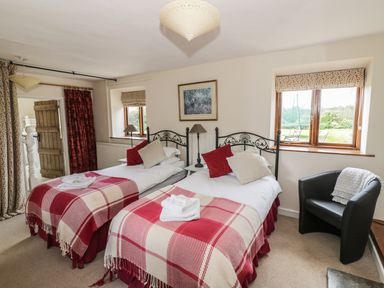A bedroom with two single beds plaid blankets and pillows a black armchair and windows at Highcroft  Stratford-Upon-Avon