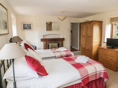 A bedroom with two single beds red and white plaid blankets wooden wardrobe and chest of drawers with a tv at Highcroft Stratford-Upon-Avon