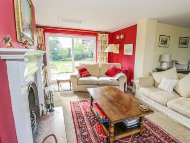 A living room with beige sofas a wooden coffee table on a red patterned rug and a white fireplace at Highcroft  in Stratford-Upon-Avon