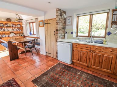A kitchen and dining area with wooden cabinets a dishwasher a dining table and chairs and a wooden plate rack at Highcroft in Stratford-Upon-Avon