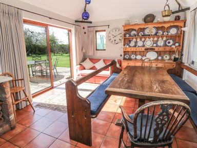 A dining room with wooden table and benches and a cabinet with plates and a clock at Highcroft Stratford-Upon-Avon