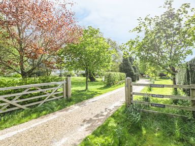 A gravel driveway with wooden gates and signs surrounded by trees and grass at Highcroft in Stratford-Upon-Avon