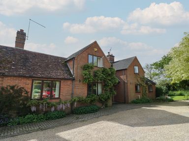A brick house with a tiled roof and climbing plants by a gravel driveway at Highcroft in Stratford-Upon-Avon
