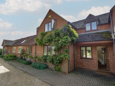 Exterior view of a brick house with plants and a paved pathway at Highcroft in Stratford-Upon-Avon