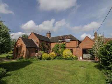 A brick house with multiple roof sections and chimneys surrounded by grass and bushes at Highcroft  Stratford-Upon-Avon