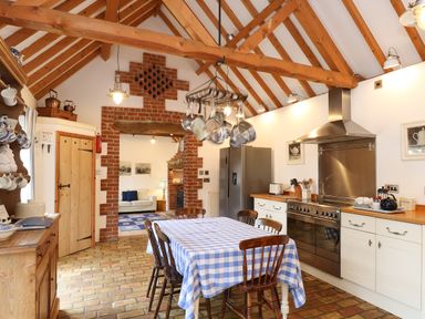 A kitchen with exposed wooden beams a dining table with a blue and white checkered tablecloth and wooden chairs at Stable Cottage in Necton near Swaffham