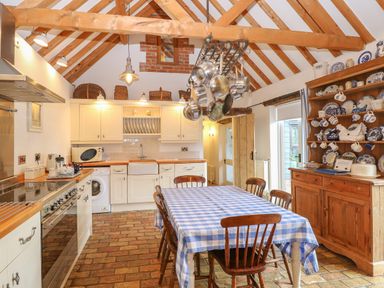 A kitchen with wooden beams pots hanging a dining table with checkered tablecloth and cupboards at Stable Cottage in Necton near Swaffham