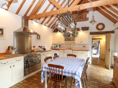 A kitchen with a dining table covered by a checkered tablecloth and hanging pots at Stable Cottage Necton near Swaffham