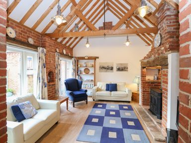 A living room with two white sofas a blue armchair a patterned rug a brick fireplace and exposed wooden beams at Stable Cottage in Necton near Swaffham