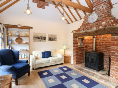 A living room with a blue armchair white sofa rug and brick fireplace at Stable Cottage in Necton near Swaffham