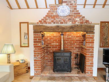 A brick fireplace with a wood stove and a wooden beam mantel with a decorative plate above at Stable Cottage in Necton near Swaffham