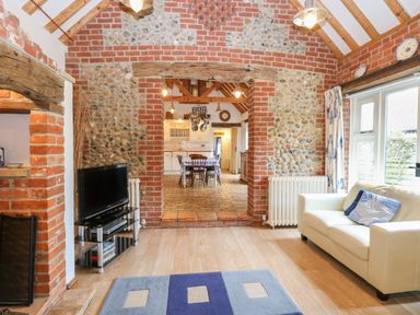 A living room with a white sofa and television facing a dining area in a brick and stone walled cottage at Stable Cottage Necton near Swaffham