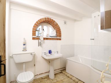 A bathroom with a toilet sink bathtub and a small arched window at Stable Cottage in Necton near Swaffham