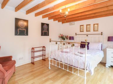 A bedroom with a white metal bed frame two bedside tables with lamps wooden beams on ceiling and framed pictures on wall at Stable Cottage in Necton near Swaffham
