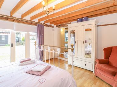 A bedroom with a bed with folded towels wardrobe with mirrored doors and an armchair at Stable Cottage in Necton near Swaffham