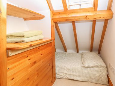 A small attic bedroom with a single bed under a skylight and folded towels on a wooden shelf at Stable Cottage in Necton near Swaffham