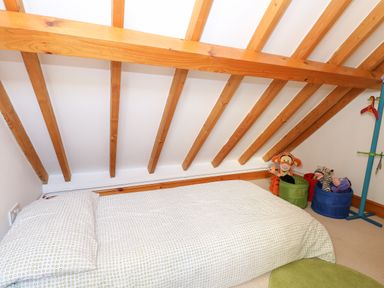 A bedroom with a single bed under a sloped wooden beam ceiling with stuffed animals in bins at Stable Cottage in Necton near Swaffham