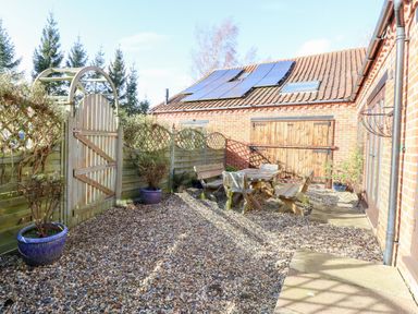 An outdoor patio area with wooden benches and table gravel ground and potted plants at Stable Cottage Necton near Swaffham