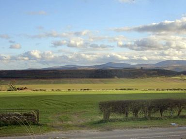 A rural landscape with green fields hedges and distant hills under a cloudy sky at The Old Farmhouse in Lowick