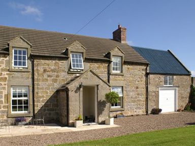 Stone house with dormer windows and a garage with a white door at The Old Farmhouse in Lowick