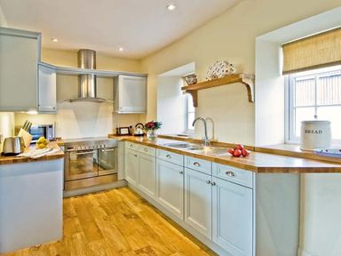 A kitchen with wooden countertops, white cabinets, double oven, stainless steel hood, and windows at The Old Farmhouse in Lowick