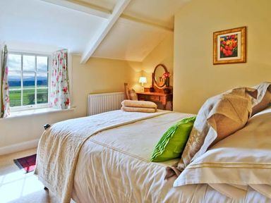 A bedroom with a bed green cushion dressing table and floral curtains at The Old Farmhouse in Lowick