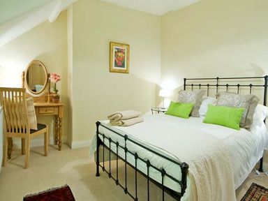 A bedroom with a black metal bed frame green pillows a wooden dressing table and chair at The Old Farmhouse in Lowick