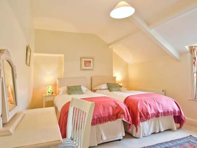 A bedroom with two single beds with red throws and green cushions a chair a desk and a mirror at The Old Farmhouse in Lowick