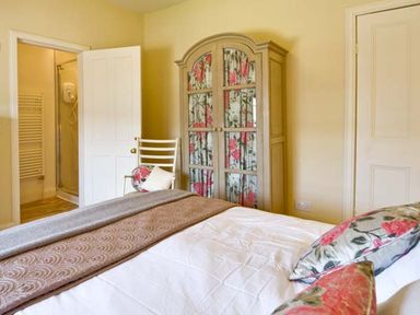 A bedroom with a bed pillows a chair and a cabinet with floral curtains at The Old Farmhouse in Lowick