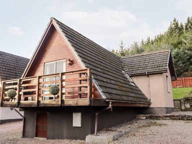 An exterior view of a wooden chalet with a balcony and sloped roof surrounded by trees at Larchfield Chalet 2 Heights of Achterneed near Strathpeffer