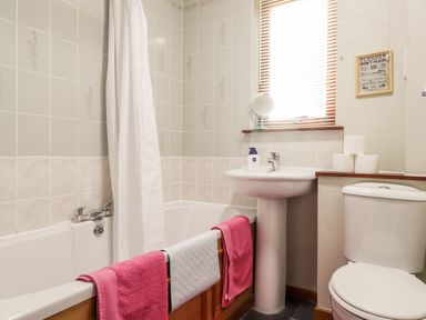 A bathroom with a bathtub towels on the tub edge a pedestal sink with soap rolls of toilet paper and a toilet at Larchfield Chalet 2 Heights of Achterneed near Strathpeffer