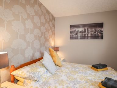 A bedroom with a wooden bed frame floral bedding and pillows bedside tables with lamps and a city skyline picture on the wall at Larchfield Chalet 2 Heights of Achterneed near Strathpeffer