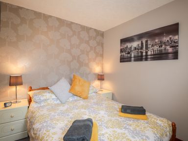 A bedroom with a bed a patterned wallpaper nightstands with lamps and a cityscape picture on the wall at Larchfield Chalet 2 Heights of Achterneed near Strathpeffer