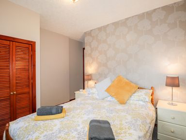 A bedroom with a bed with yellow and gray bedding two bedside tables with lamps and a wooden closet door at Larchfield Chalet 2 Heights of Achterneed near Strathpeffer