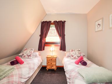 A bedroom with two single beds and a window with curtains at Larchfield Chalet 2 Heights of Achterneed near Strathpeffer