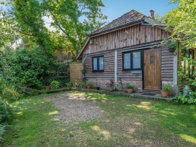 A wooden cabin with a tiled roof and potted plants outside in a garden setting at Endymion Linwood near Ringwood New Forest