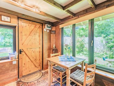 A dining area with a wooden table and two chairs near large windows and a wooden door at Endymion Linwood near Ringwood New Forest