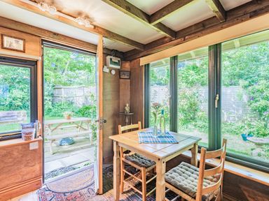 A dining area with a wooden table and chairs next to large windows and a door opening to a garden at Endymion Linwood near Ringwood New Forest