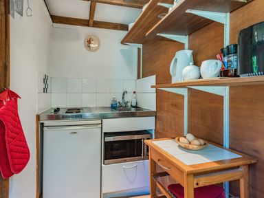 A small kitchen area with a sink stove refrigerator microwave wooden shelves and a small table at Endymion Linwood near Ringwood New Forest
