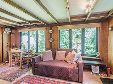A sitting room with a sofa and cushions beside windows and a wooden dining table with chairs at Endymion in Linwood near Ringwood New Forest