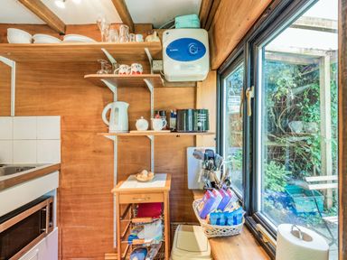 A small kitchen area with wooden shelves and counter next to a window showing an outdoor garden at Endymion in Linwood near Ringwood New Forest