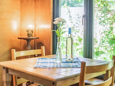 A wooden dining table with chairs a blue checkered cloth a bottle and a vase with flowers near a window at Endymion in Linwood near Ringwood New Forest