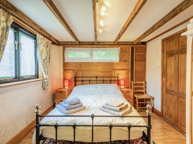 A bedroom with a metal bed frame two bedside tables with lamps wooden chair and a window at Endymion Linwood near Ringwood New Forest