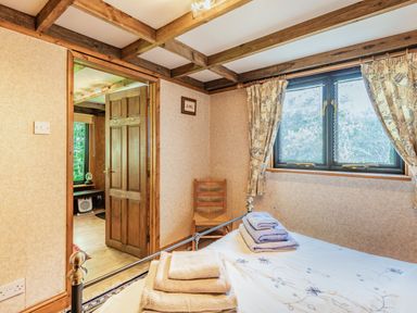 A bedroom with a bed covered with folded towels a wooden chair and a window with floral curtains at Endymion Linwood near Ringwood New Forest